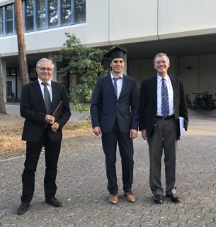 Auf dem Foto sind Prof. Lenz, Peter Schwab und Prof. Meyer-Wegener nach der Promotionsprüfung zu sehen. Sie stehen draußen, vor dem Eingang des Informatik-Hochhauses. Alle drei Männer stehen nebeneinander und tragen legere dunkle Anzüge. Peter Schwab ist in der Mitte und hat einen Doktorhut auf. Alle drei lächeln in die Kamera.